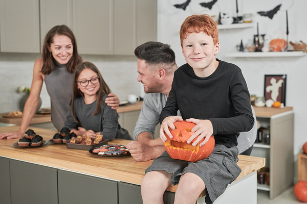 Boy Holds Halloween Pumpkin while His Family Talks